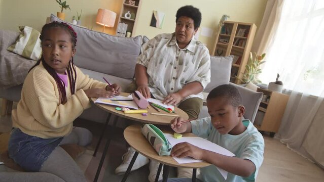 African American senior adult woman and her two tween grandchildren drawing together at daytime in cozy living room