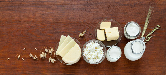 Rustic still life with fresh dairy products - milk, cottage cheese, yogurt, sour cream, butter and oat ears on wooden table. Organic farm food. Place for text. Banner. Flat lay, copy space, mock up
