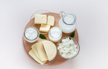 Top view of fresh dairy products: milk in a jug, cottage cheese, yogurt, sour cream and butter on a wooden round podium on a light background. Organic farm natural healthy food. Flat lay, close-up