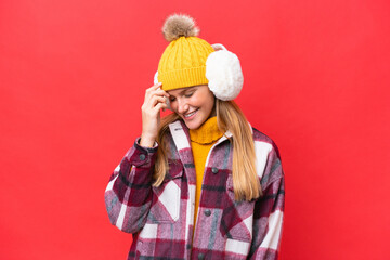 Young beautiful woman wearing winter muffs isolated on red background laughing