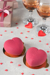 Fototapeta premium Homemade bright mousse cakes Hearts with pink velor coating and two glasses of rose wine for Valentine's Day, Vertical image