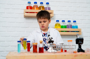Young boy practice as young or junior scientist hold colored test tube and study in science class...