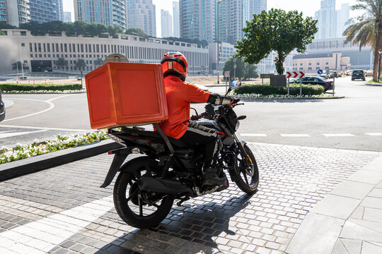 A food delivery courier is driving an order to a customer's home on a moped. takeaway food during quarantine. transport delivery of parcels at home. motorcycle rider with a big backpack