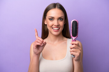 Young caucasian woman holding hairbrush isolated on purple background pointing up a great idea