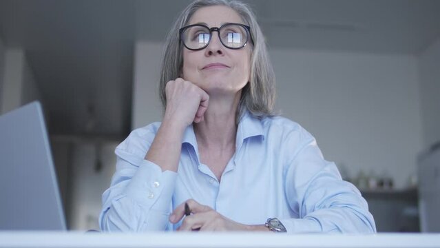 Senior lady procrastinating on work, looking at window instead of working laptop