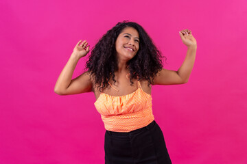 Curly-haired woman in summer clothes on a pink background dancing, studio shot