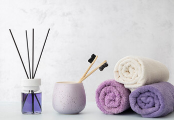 Obraz na płótnie Canvas Aroma diffuser, bamboo toothbrushes in the cup, stack of bath towels on the bright table against white wall