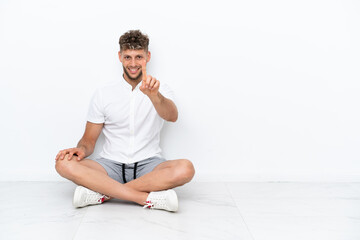 Young blonde man sitting on the floor isolated on white background showing and lifting a finger