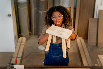 Top view of Asian wood worker or carpenter woman hold wooden chair and check quality of product in factory workplace.