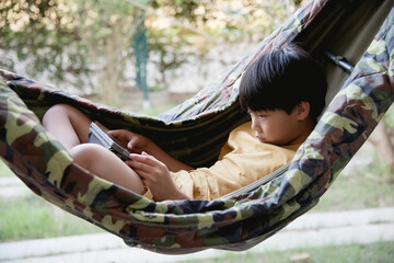 Little asian boy using a tablet computer while relaxing in a hammock