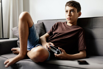 Teenager playing video games at home. Teenager sitting on sofa playing video game with bad posture....