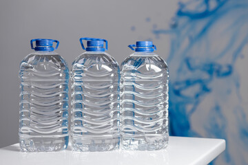 Three full 5 liter bottles of water on a white table on a gray background. Water delivery
