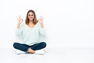 Young caucasian woman sitting on the floor isolated on white background showing an ok sign with fingers