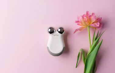 microcurrent facial toning device on color background with flower. anti-aging and face lifting...