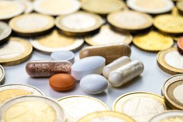 Lozenges and tablets, with coins around them. Costs of medicines, medical therapies and health. Pharmaceutical price increases.
