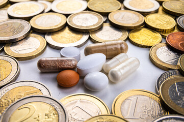 Lozenges and tablets, with coins around them. Costs of medicines, medical therapies and health. Pharmaceutical price increases.
