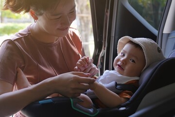 A young Asian mother Takes care a baby boy in the car seat. Family car, Childcare. Baby Travel Safety first. Play with child in car.