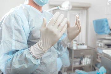 Surgeon holds hands up disinfected hands in white gloves before surgery
