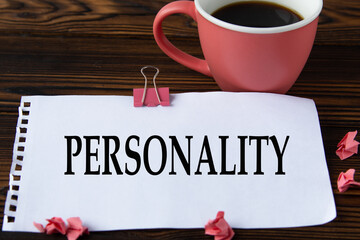 PERSONALITY - word on a white sheet on a wooden brown background with a cup of coffee and a pen