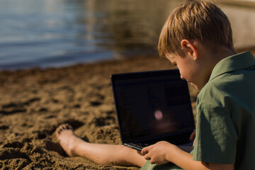 Kid with computer on beach near the sea
