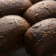 Loaves of dark rye bread with malt. Loaves in shape of bricks, sprinkled with sesame seeds on grate. Top view, close-up. High quality photo
