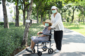 Obraz na płótnie Canvas Caregiver help and care Asian senior or elderly old lady woman patient sitting on wheelchair and wear a face mask to travel in park,