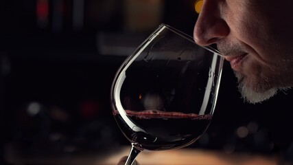 Fototapeta Close up man smelling red wine in wine glass. Wine expert tasting, rating and drinking wine, bottles in background. obraz