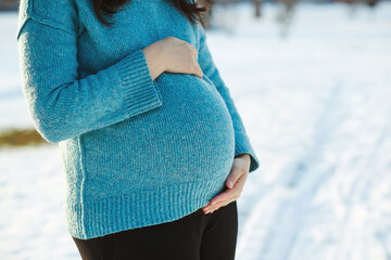 Pregnant woman in blue sweater touching big belly with hands. Warm clothes in cold weather. Pregnancy time.
