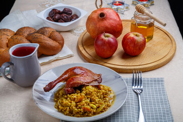 Spelled with duck leg in a plate on the table for Rosh Hashanah next to pomegranate honey apples wine and challah on a white tablecloth and candles.