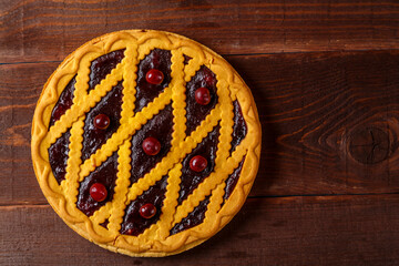 Cherry shortcrust pastry pie decorated with cherry berries and pastry grill on a wooden table.copy space