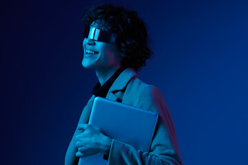 Portrait of a male hacker with a laptop and futuristic glasses in blue light, Blue Perennial color, cyber security, technology, laptop copy space, template, trendy neon, freelance online work