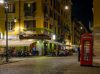 Fototapeta na wymiar Old street with restaurant tables Milan, Italy. Night cityscape of Milan. Architecture and landmarks of Milan.