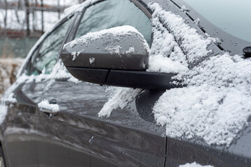 A car covered with snow. The onslaught of winter and snow for motorists. Snow on the car, windshield, car mirrors.