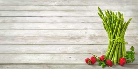 Bunch of green raw asparagus decorated with fresh strawberries on bright wide wood background as copy space