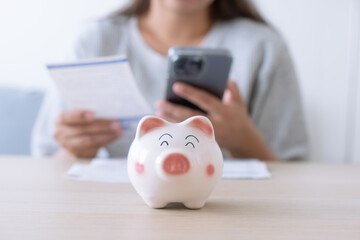 Woman pay household expenses using mobile phone and save money in piggy bank