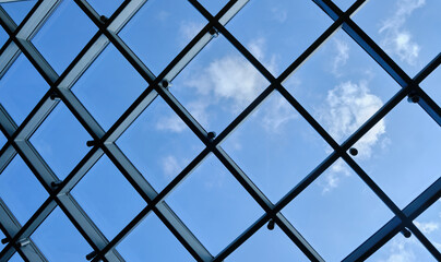 Below view of glass roof consisting of square segments with sky visible through