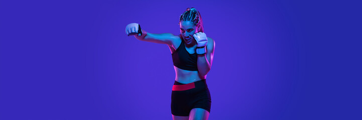 Boxing. Young woman athletic female MMA fighter training isolated on gradient blue-pink background...