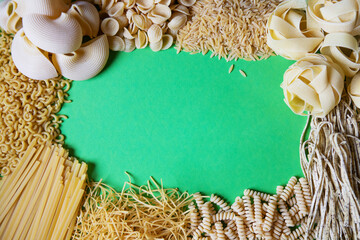 Various types of dry pasta with copy space on green background