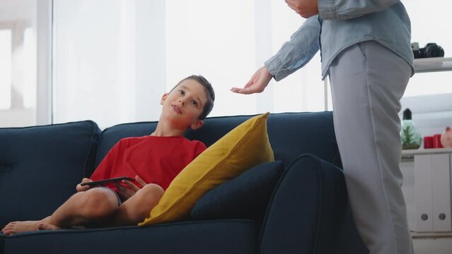 Mother taking away little son's tablet and giving him book instead, parenting
