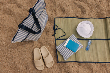 Fototapeta na wymiar Close-up of lining with bag, slippers, sunglasses, panama hats on sand. Beach accessories are laid out on mat.