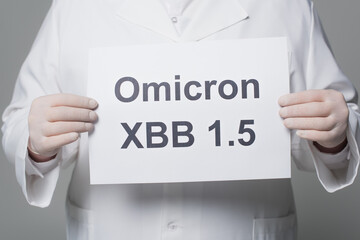 Cropped view of scientist in white coat and latex gloves holding paper with omicron xbb lettering isolated on grey.