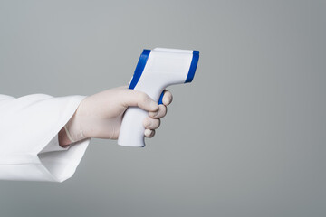Cropped view of doctor in latex glove holding non-contact pyrometer isolated on grey.