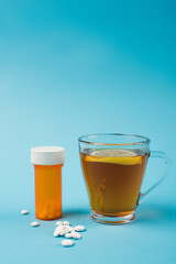 Pills near cup of tea with lemon on blue background.