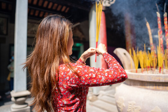 Vietnamese girl in traditional long dress or Ao Dai dress is praying with incense stick in the burning pot of a pagoda in Ho Chi Minh City, Vietnam. Tet holiday and New Year.