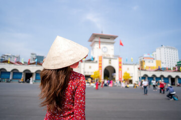 Vietnamese girl with Ao Dai dress walking in front of Ben Thanh market , Ho Chi Minh city, Vietnam....