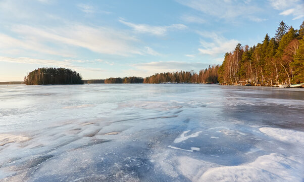 Panoramic view of the forest lake on a sunny winter day. Evergreen trees. Soft sunlight. Frozen water surface. Finland. Environment, nature, ecology, ecotourism, cold weather, climate change themes