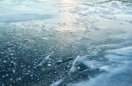 Cracked ice, snowflakes, snow, water surface, frozen lake shore. Sunset or sunrise. Texture, close-up. Winter scenery. Concept image, graphic resources. Nature, ecology, climate, global warming