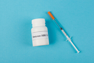 Top view of pills with omicron xbb lettering near syringe on blue background.