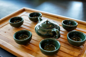 Set of 2 black pottery pots with 6 cups on a wooden tray. Soft and selective focus.    