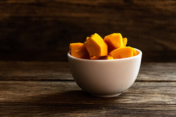 Sliced pumpkin in a white bowl on a wooden table.